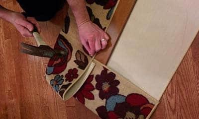 building a cat scratching board Woman hammering tack nails into board to secure a flowered area rug to wood for cat scratch board.